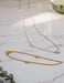 Two necklaces on a marble surface, one gold with heart pendants and one silver.