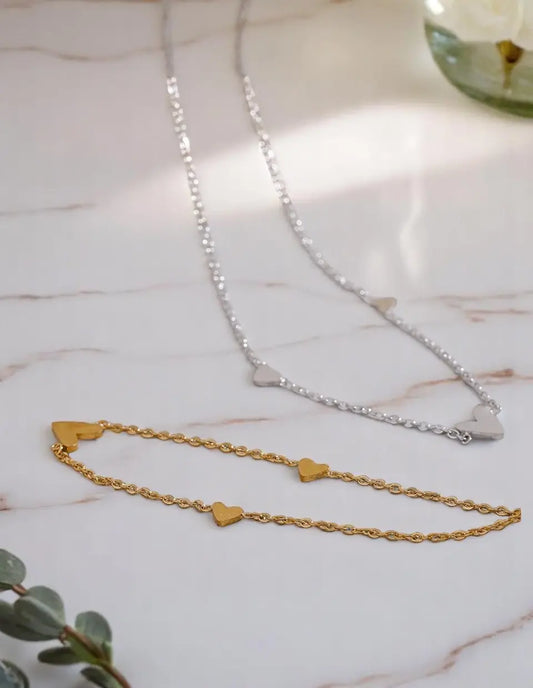 Two necklaces on a marble surface, one gold with heart pendants and one silver.