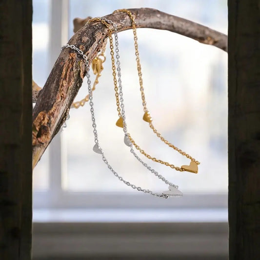 Three gold and silver necklaces hanging on a branch with a blurred natural background