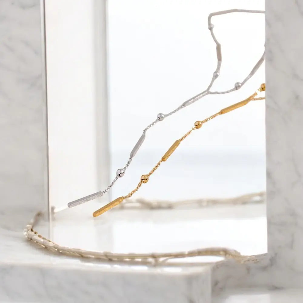 Gold and silver necklace on a clear stand with a marble background