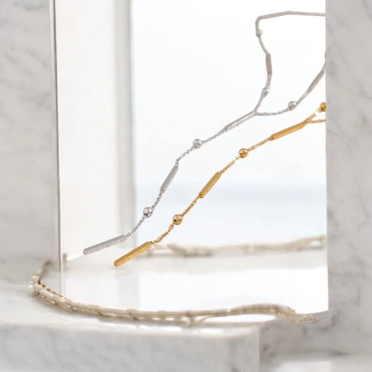 Gold and silver necklace on a clear stand with a marble background