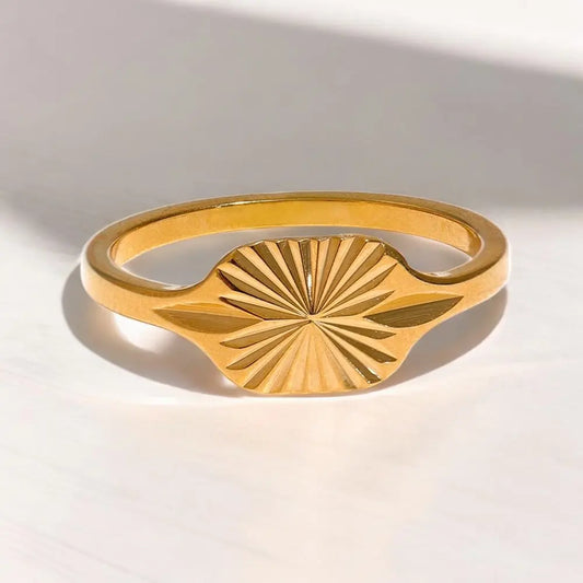 Gold ring with a sunburst design on a light gray background