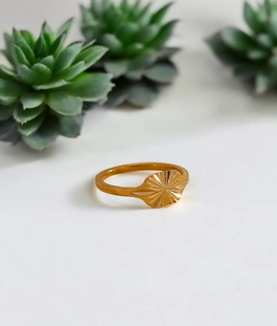Gold ring with sunburst design on a white surface with succulents in the background