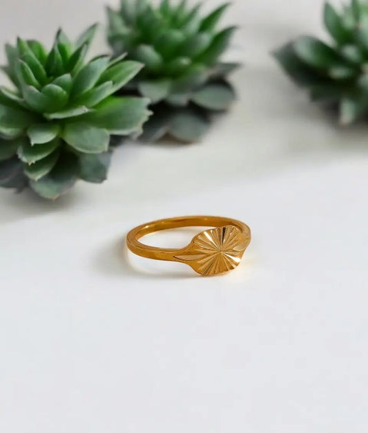Gold ring with sunburst design on a white surface with succulents in the background