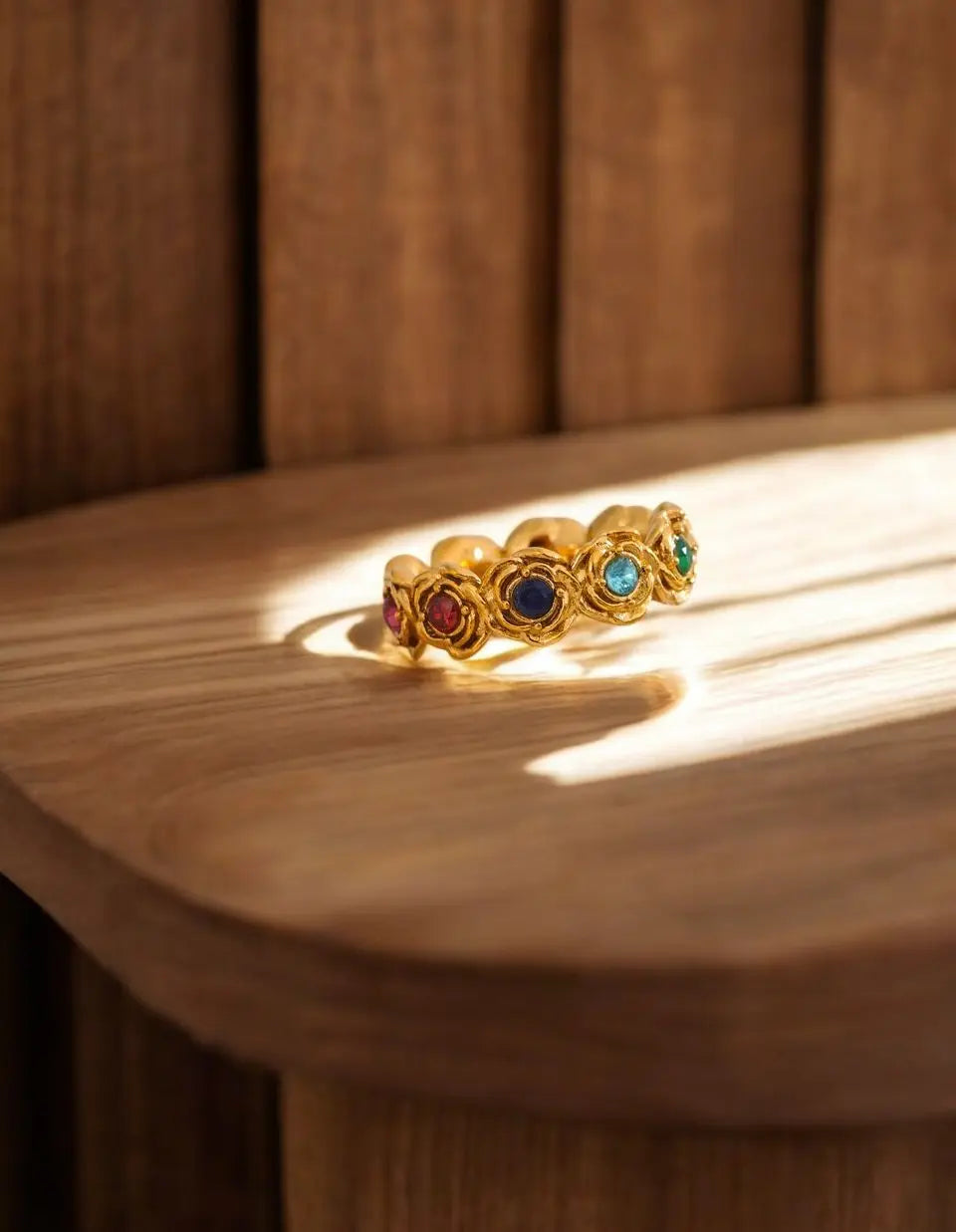 Gold ring with colored gemstones on a wooden surface