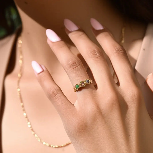 Close-up of a hand wearing a gold ring with gemstones, with a blurred background.