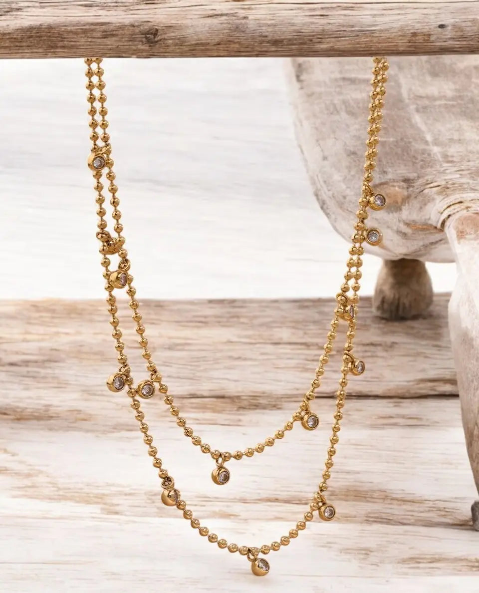 Gold beaded necklace on a wooden surface with a neutral background