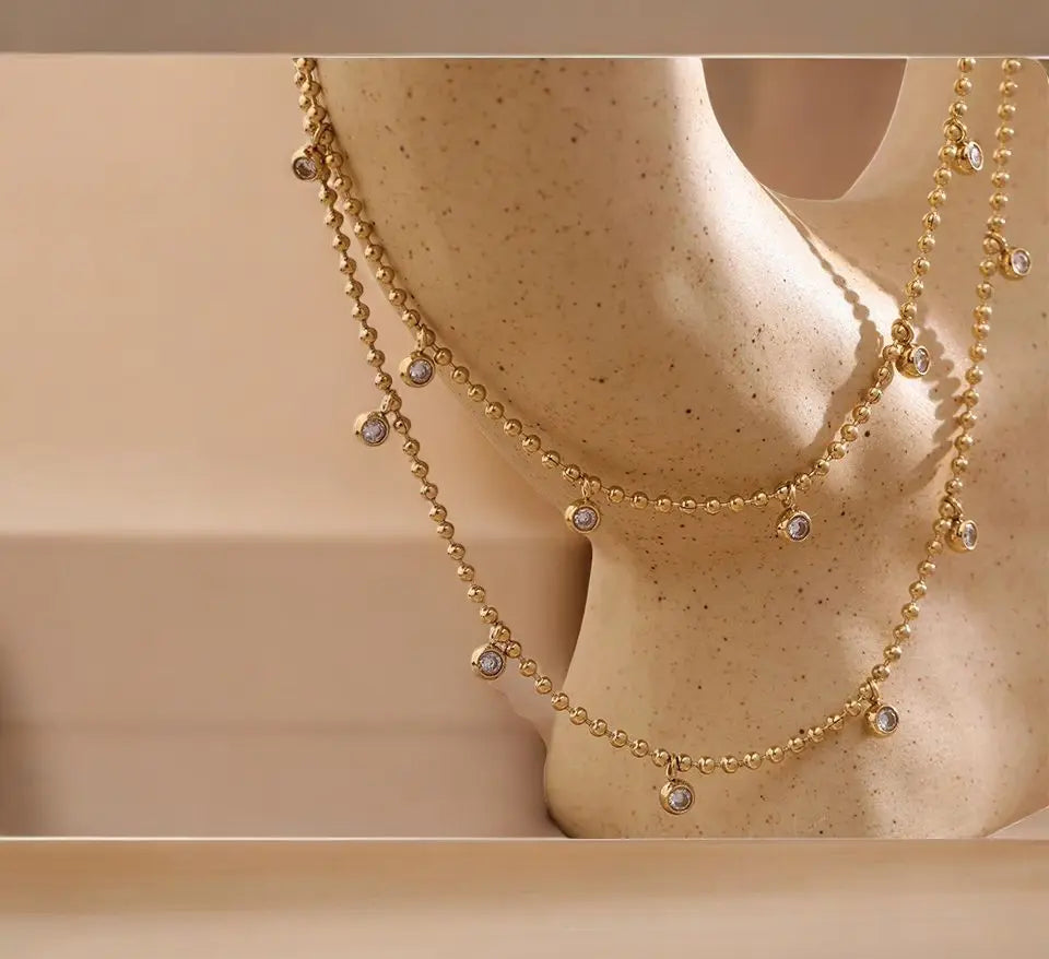Gold necklace with small beads on a mannequin bust.