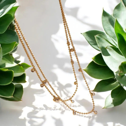 Gold necklace on a white surface with green leaves in the background