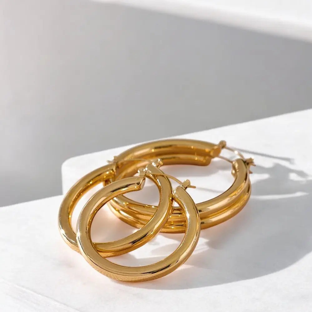 Gold hoop earrings on a white surface with soft shadows