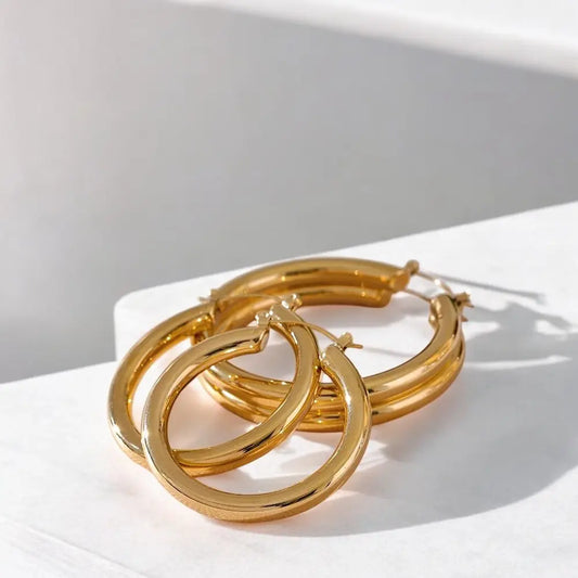 Gold hoop earrings on a white surface with soft shadows