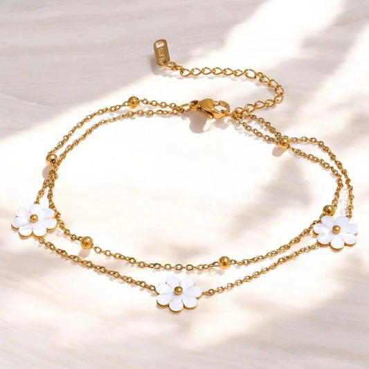 Gold chain bracelet with white flower charms on a light background