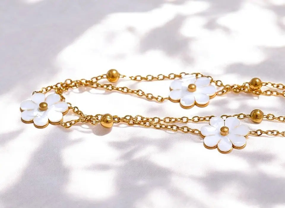 Gold chain necklace with white flower pendants on a light background