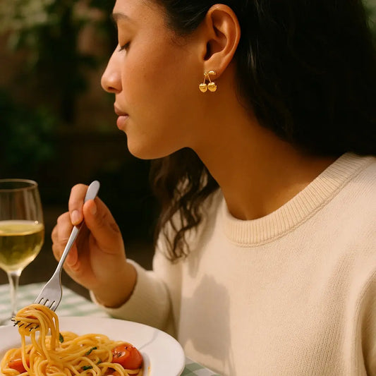 Woman eating spaghetti with a glass of white wine, wearing gold earrings.