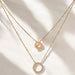 Two gold necklaces with circular pendants on a light background