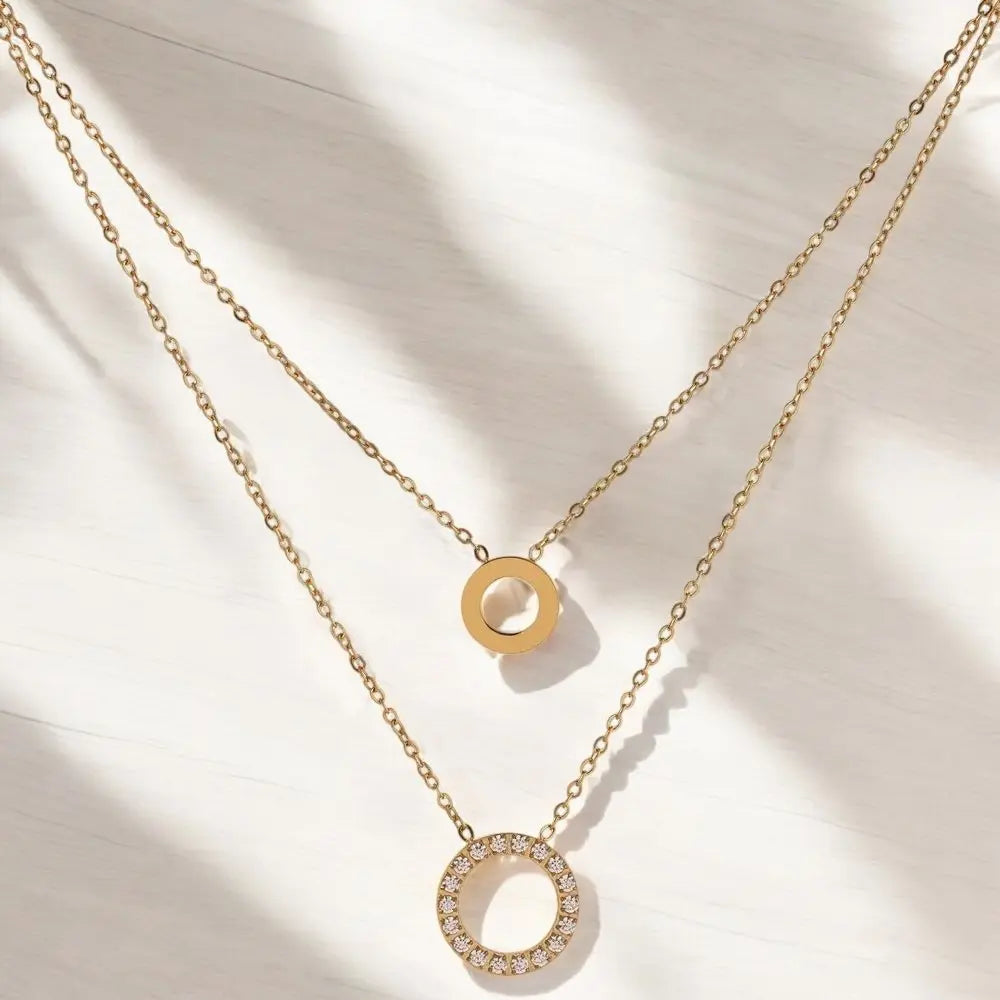 Two gold necklaces with circular pendants on a light background