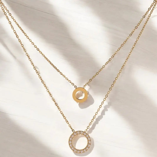 Two gold necklaces with circular pendants on a light background