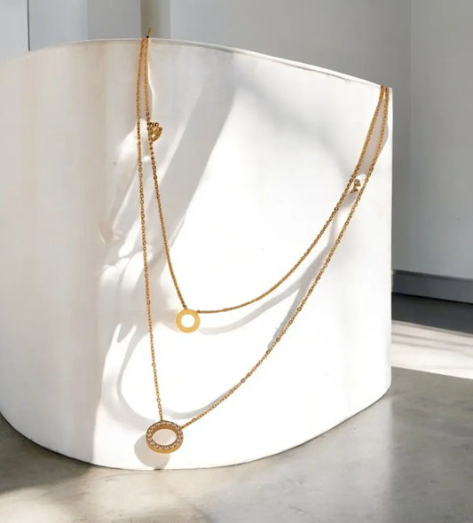 Two gold necklaces on a white cylindrical object with a neutral background