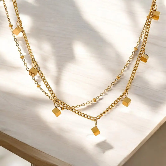 Gold chain necklace with square pendants on a light background