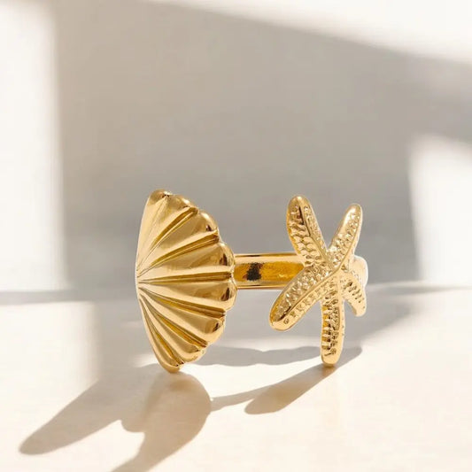 Gold ring with shell and starfish design on a light background