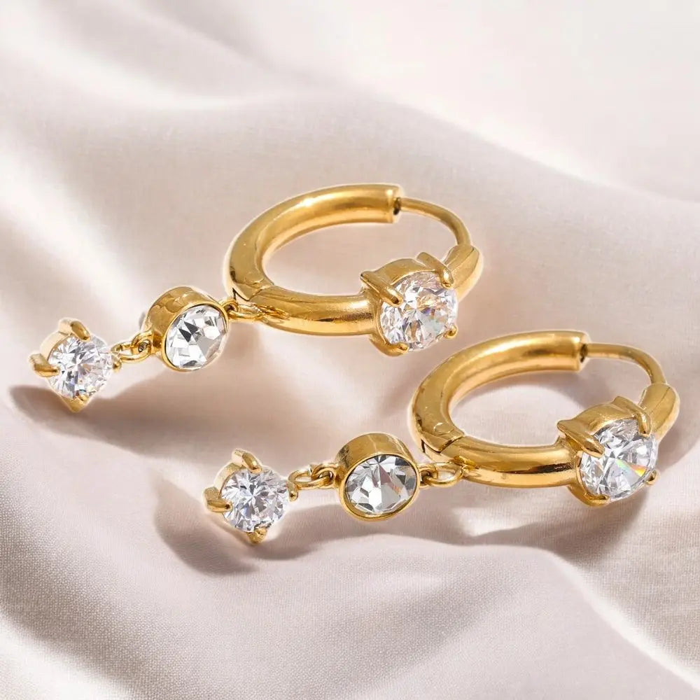 Gold hoop earrings with clear gemstones on a beige fabric background
