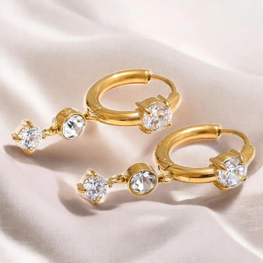 Gold hoop earrings with clear gemstones on a beige fabric background