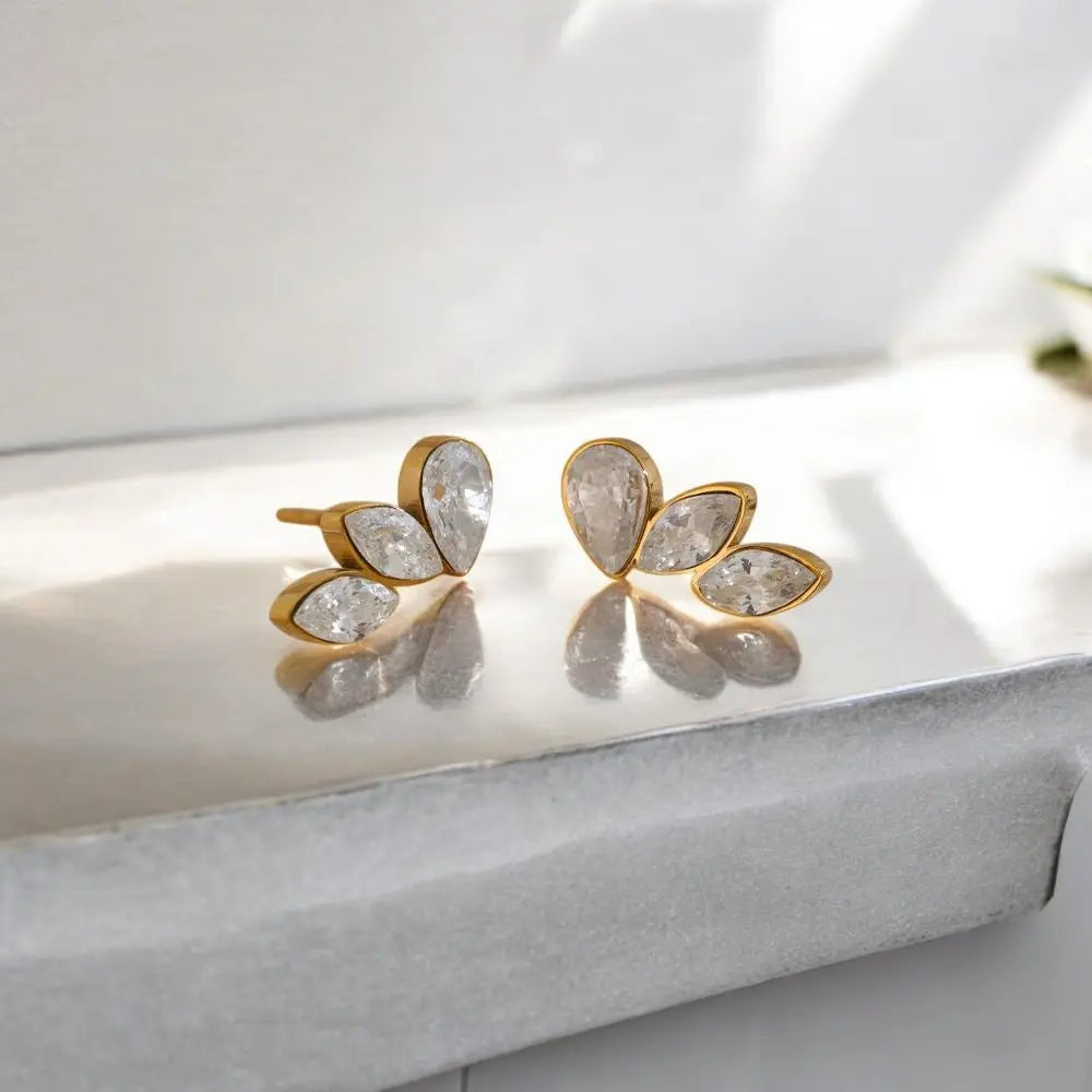 Gold and crystal earrings on a reflective surface