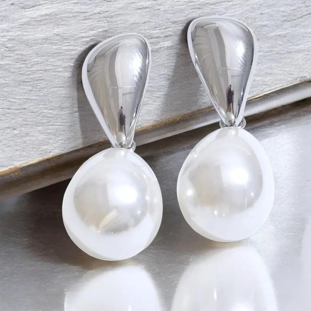 Pearl earrings with silver teardrop clasps on a light wooden surface