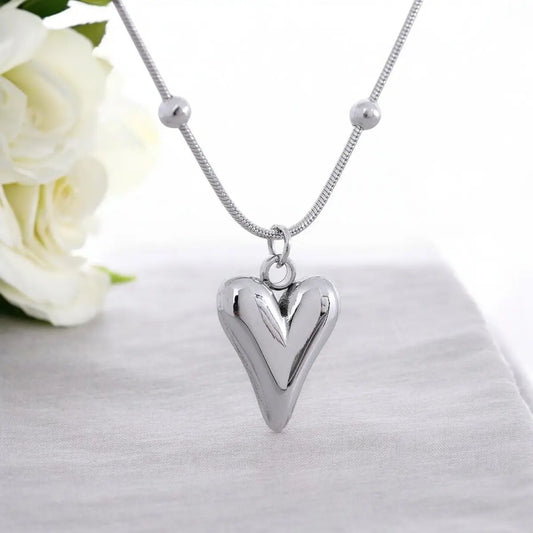 Silver heart-shaped pendant necklace on a white background with white flowers.