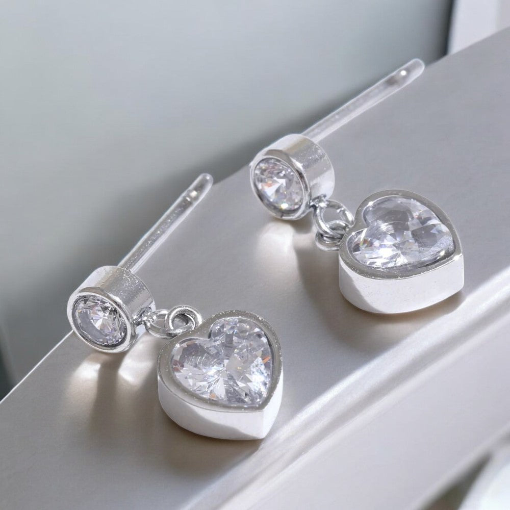 Heart-shaped silver earrings with clear gemstones on a light surface