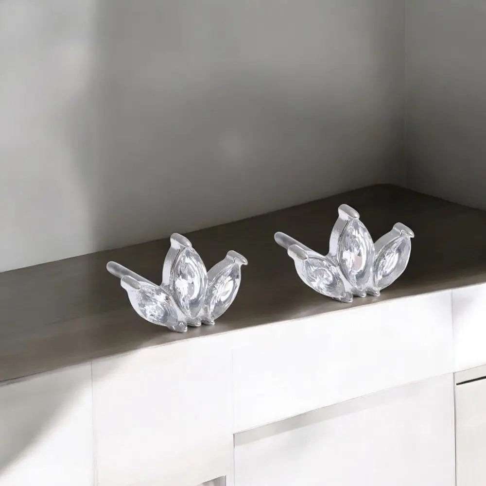 Two crystal peacock decorations on a reflective surface with a neutral background