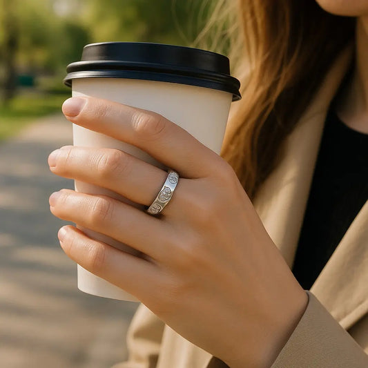 Hand holding a white paper cup with a black lid outdoors