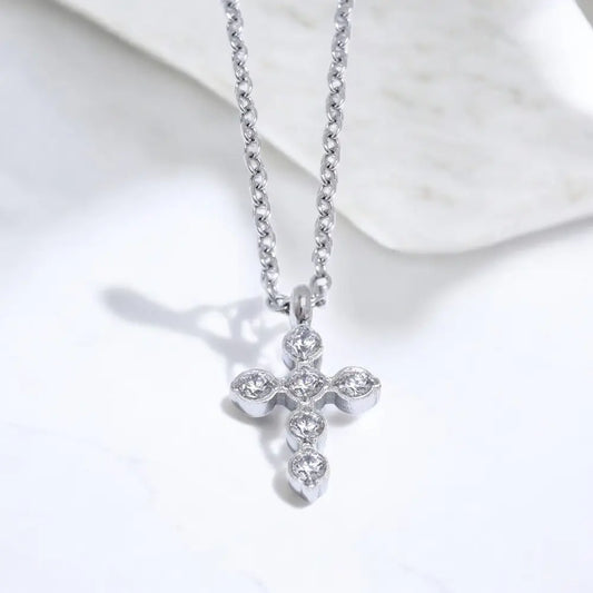 Silver cross necklace with clear stones on a white marble surface