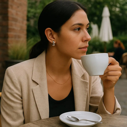Woman sitting outdoors, holding a white mug and looking thoughtful.