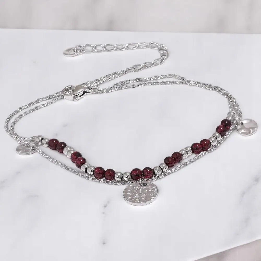 Silver necklace with red beads on a white marble surface