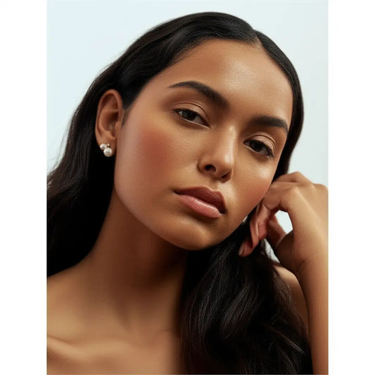Woman with long dark hair and pearl earrings against a light background