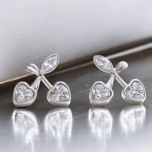 Pair of silver heart-shaped earrings with clear gemstones on a reflective surface.