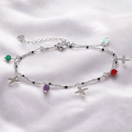 Silver anklet with colorful beads and starfish charms on a white fabric background