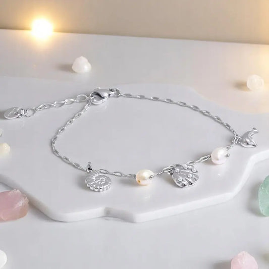 Silver anklet with pearls and charms on a white surface