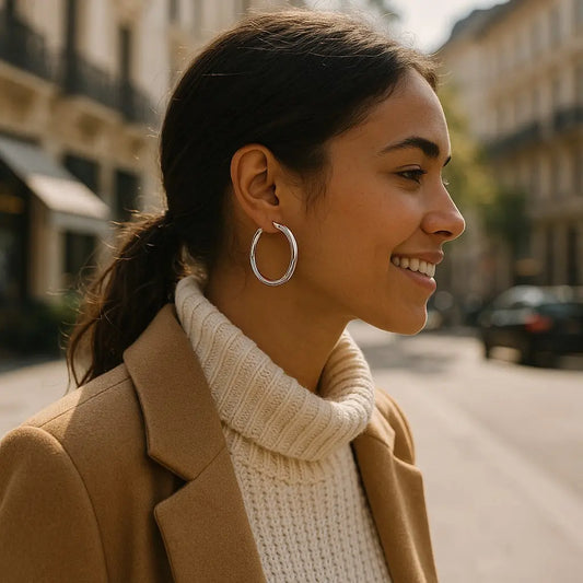 Woman wearing a beige coat and white turtleneck with hoop earrings on a street.