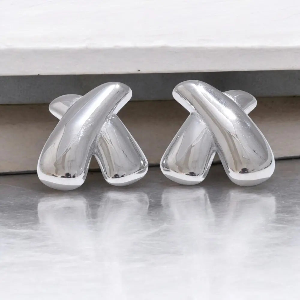 Two silver abstract sculptures on a reflective surface with a neutral background