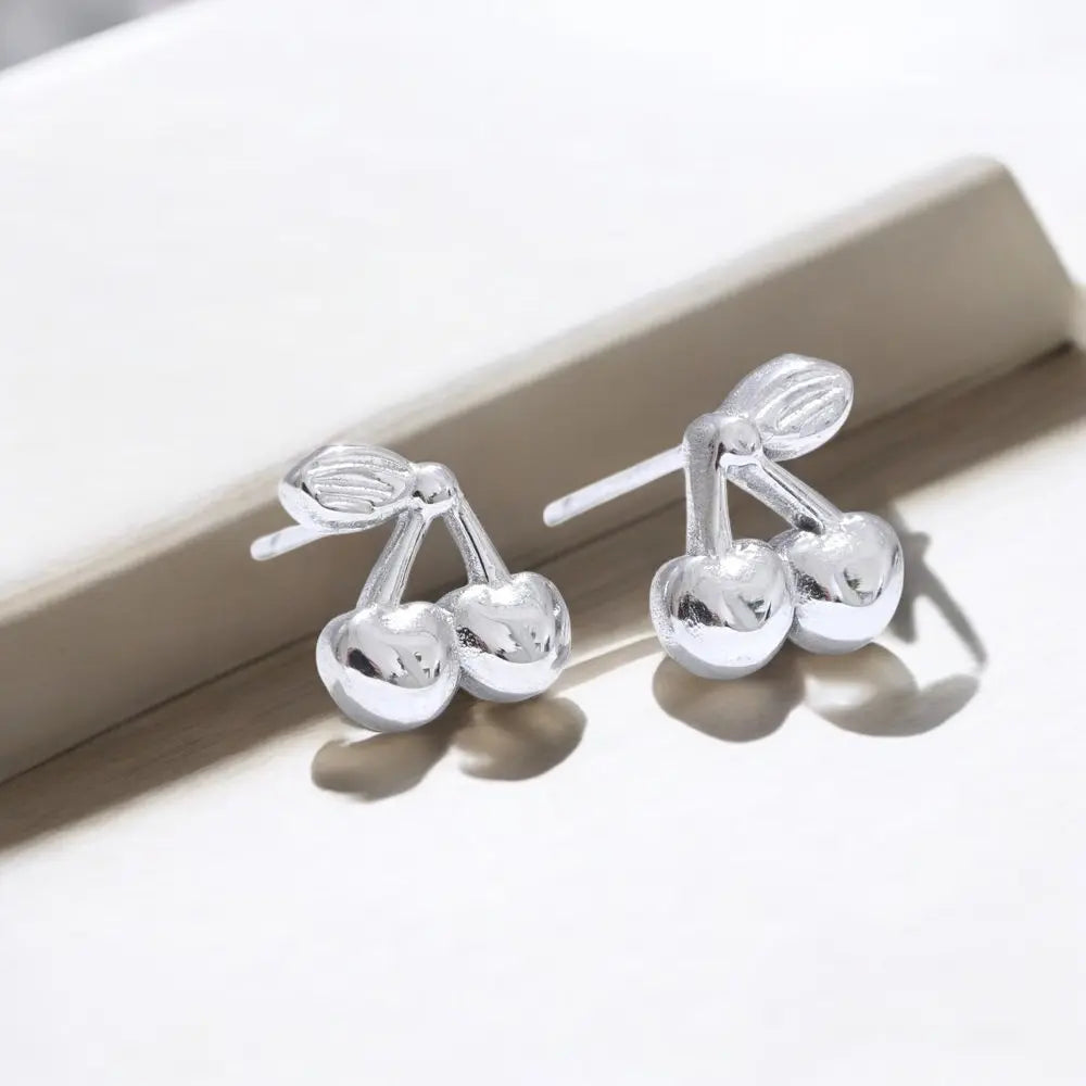 Silver cherry-shaped earrings on a light background