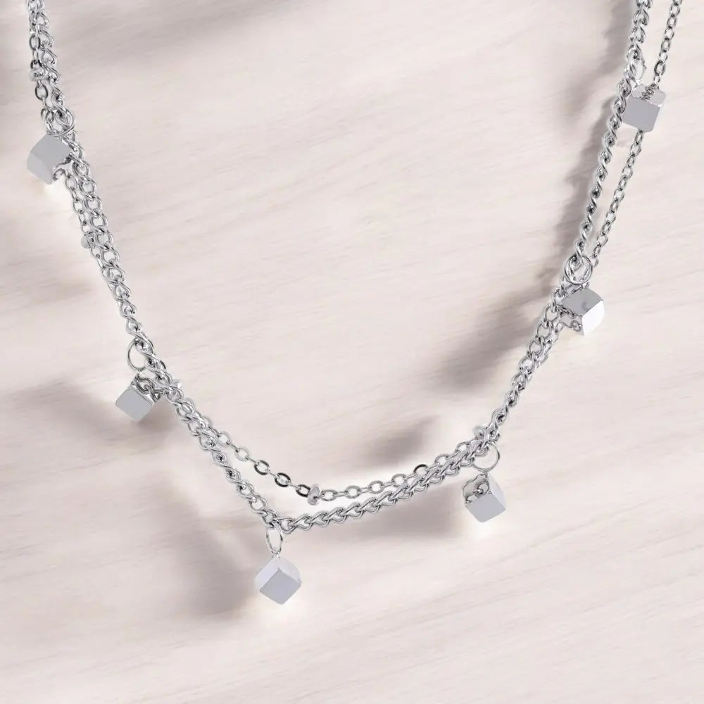 Silver chain necklace with square pendants on a light pink background