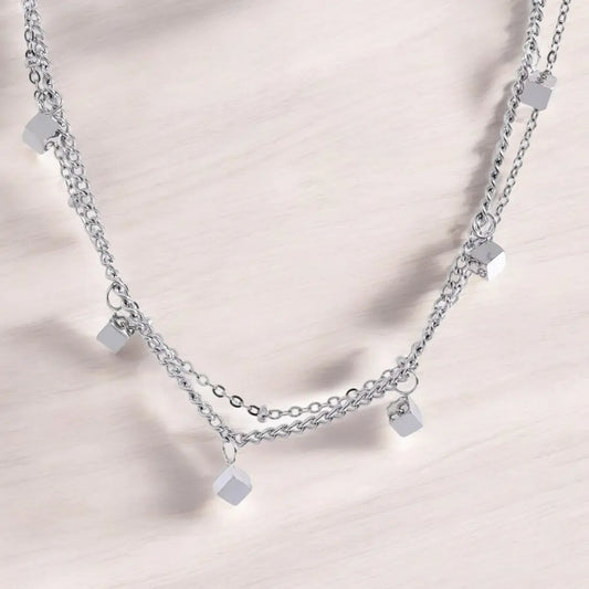 Silver chain necklace with square pendants on a light pink background