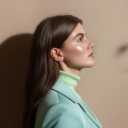 Woman wearing a light green coat and green sweater against a beige wall