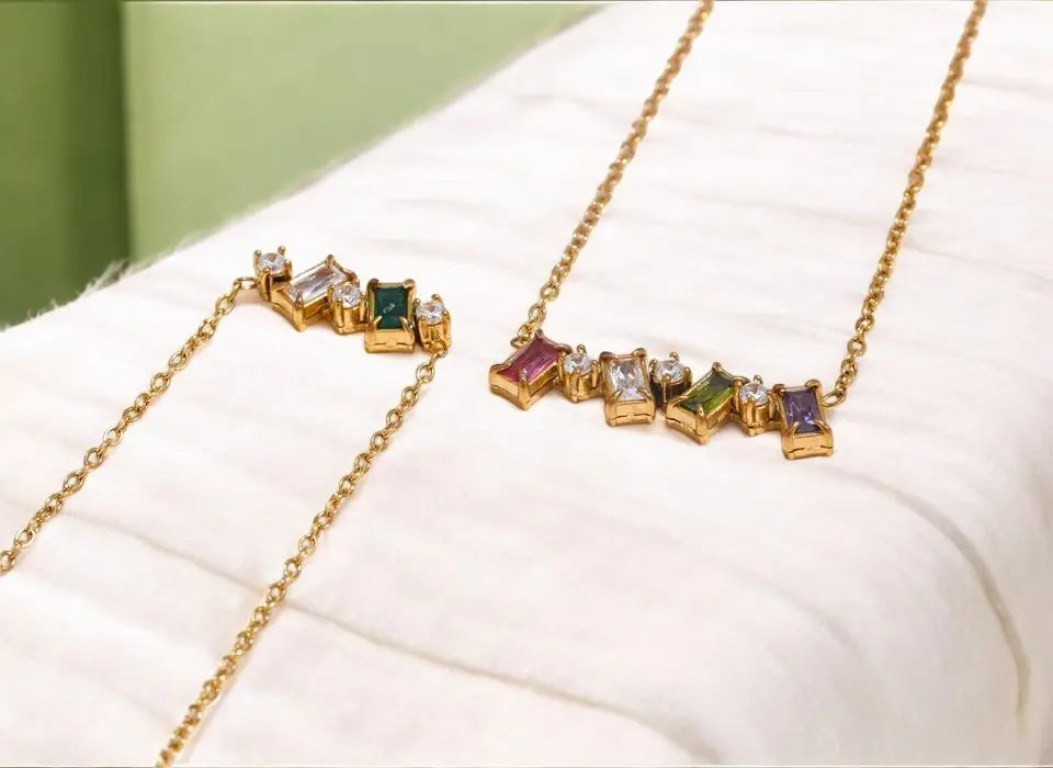 Two gold necklaces with gemstones on a white surface