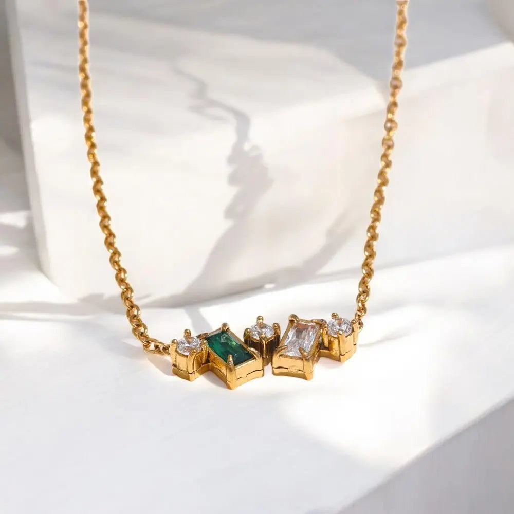 Gold necklace with green and clear gemstones on a white background