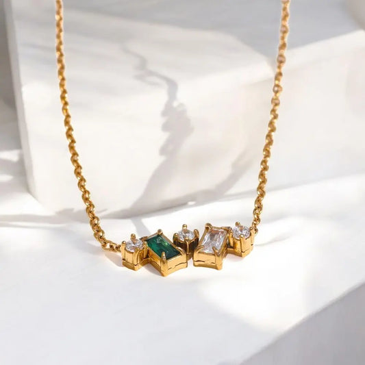 Gold necklace with green and clear gemstones on a white background