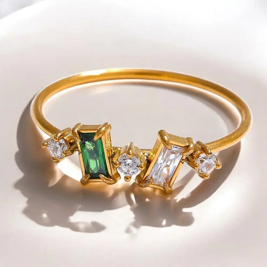 Gold bracelet with green and clear gemstones on a light background