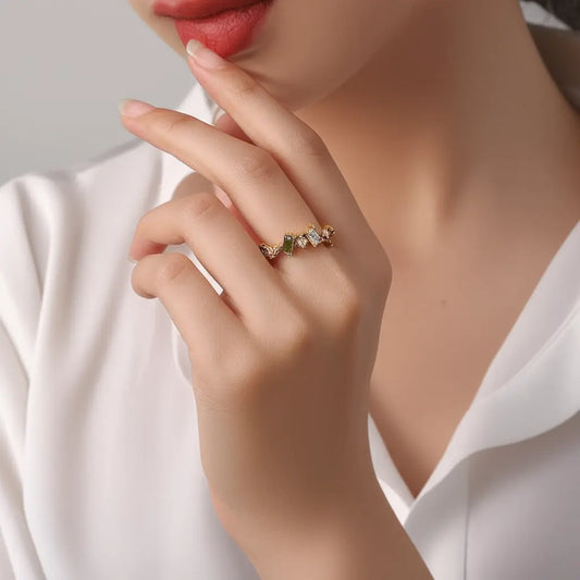 Close-up of a hand wearing a ring with green gemstones on a neutral background